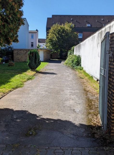 Blick auf die Verkaufsfläche und Nachbarbebauung - Befestigte Zufahrt zwischen Wohnhäusern in einem Wohngebiet