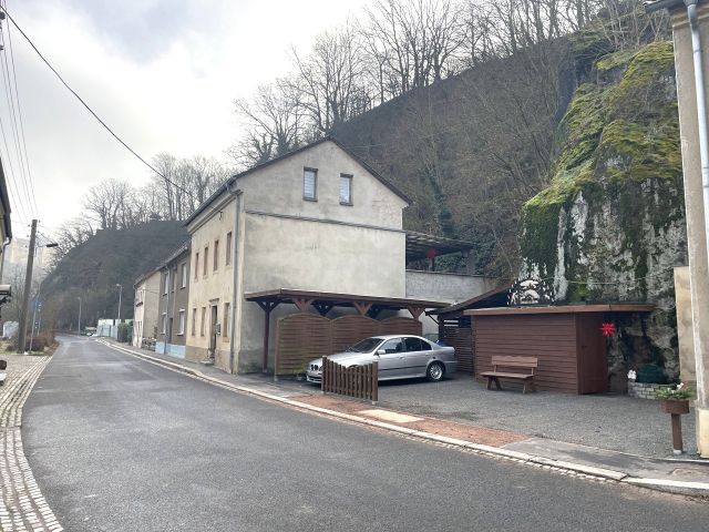 Blick auf die Verkaufsfläche mit davorliegender Wohnbebauung - Vertragsfreier Steilhang (Wald-/Gehölzflächen) hinter Wohnbebauung